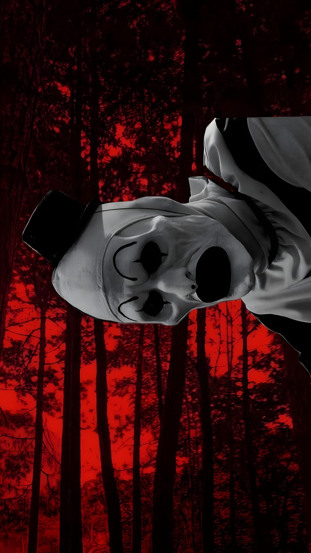 a creepy mask hanging from the side of a tree in front of a red sky Halloween Terrifier black