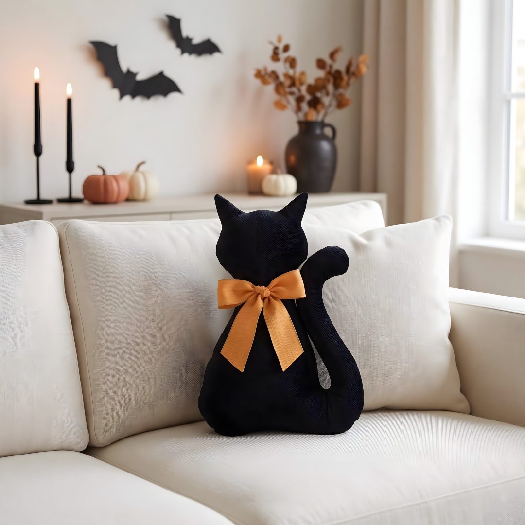 a black cat sitting on top of a white couch next to candles and pumpkins Halloween Black Cat Pillow silver