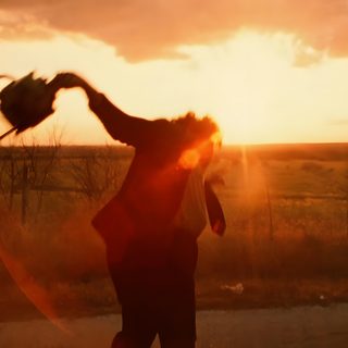 a person standing on the side of a road with their arms in the air while the sun is setting Texas Chainsaw Man Movie Halloween Orange Horror Movie, Slasher Movie Gif, Texas Chainsaw 3d 2013, saddle brown