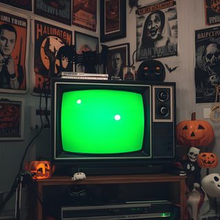 a green television sitting on top of a wooden table in front of halloween posters and pumpkins Vhs Halloween Halloween, Neon, Halloween Vhs Aesthetic, Haunted House, Spooky Screen, dark slate gray