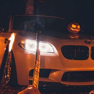 a white car with pumpkins on the hood in front of it and two jack - o'lanterns Bmw Halloween Car With Halloween Pumpkins At Night, Diy Halloween Pumpkin Display, Halloween Car Decoration, dark slate gray