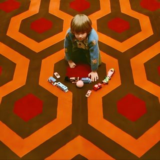 a person sitting on the floor in front of a carpet with hexagons The Shining Laptop Halloween The Shining Carpet Room, Shining Carpet, The Shining Carpet Hd, saddle brown