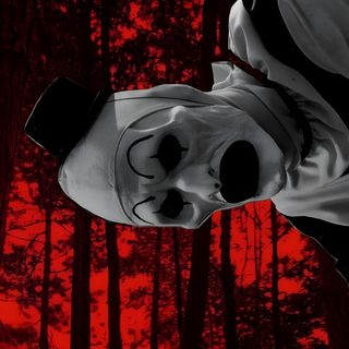a creepy mask hanging from the side of a tree in front of a red sky Halloween Terrifier black