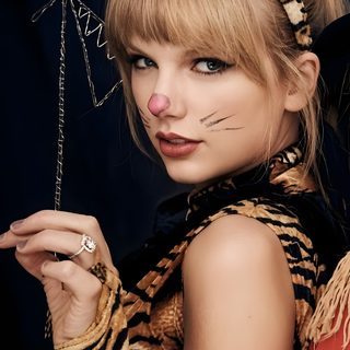 a woman with cat ears and makeup holding a string in her hand while wearing a tiger costume Taylor Swift Halloween saddle brown