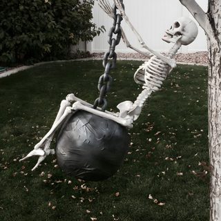 a skeleton sitting on top of a black ball in the grass next to a tree Wrecking Ball Halloween Skeleton Pics, Halloween Diy Outdoor, Halloween Outside, dark slate gray