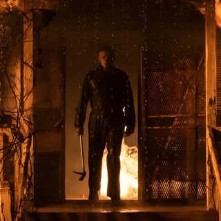 a man standing in front of a door with fire coming out of the building behind him Halloween 2018 Michael Myers Michael Myers Scenes, Michael Myers House On Fire, Michael Myers In Fire, maroon