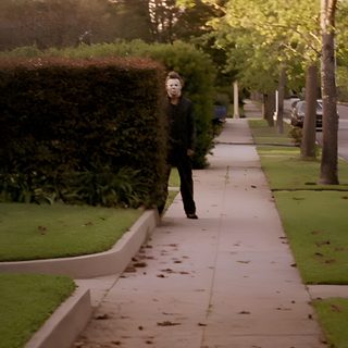 a man walking down a sidewalk next to a lush green park Halloween 1978 Horror Movie Scenes, The Babadook, Halloween 1978, Halloween Film, dark olive green