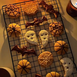 cookies are arranged on a cooling rack next to a candle Halloween Cookie Halloween Town, Halloween Aesthetic Treats, Halloween Cookies, 2000s Food, saddle brown