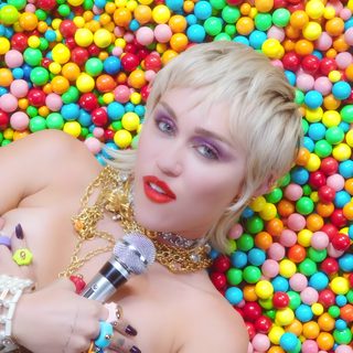 a woman laying on top of a pile of gummy balls with her mouth open Wrecking Ball Halloween Midnight Sky Miley Cyrus Lyrics, Wrecking Ball Cyrus, Miley Cyrus Flowers Music Video, dark khaki