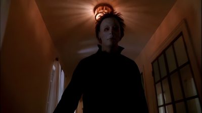 a person standing in a room with a light on above their head and an open door behind them Halloween H20 Michael Myers Scenes, Michael Myers Standing Still, Michael Myers House On Fire, black