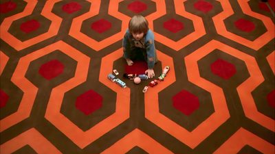 a woman sitting on the floor in front of a carpet with hexagons The Shining Laptop Halloween The Shining Carpet Room, The Shining Hotel Hallway Gif, The Shining Carpet Hd, saddle brown