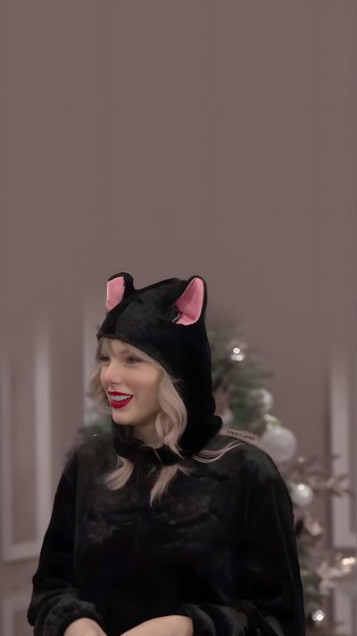 lady in black cat costume with pink ears on her head and hands folded out to the side Taylor Swift Halloween Taylor Swift Halloween Pictures, Halloween Taylor Swift, Taylor Swift Cat Photo, dim gray