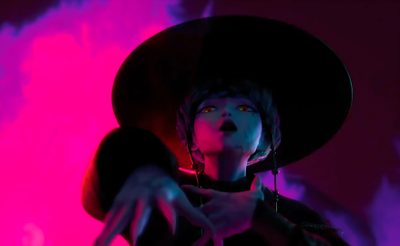 a woman wearing a black hat and holding her hand out to the side while standing in front of a pink background Baby Saja Halloween Kpop Demon Hunters Mystery Saja Concept Art, Demon Baby Kpop Demon Hunters, Baby Saja Kpop Demon Hunters Demon Form, black