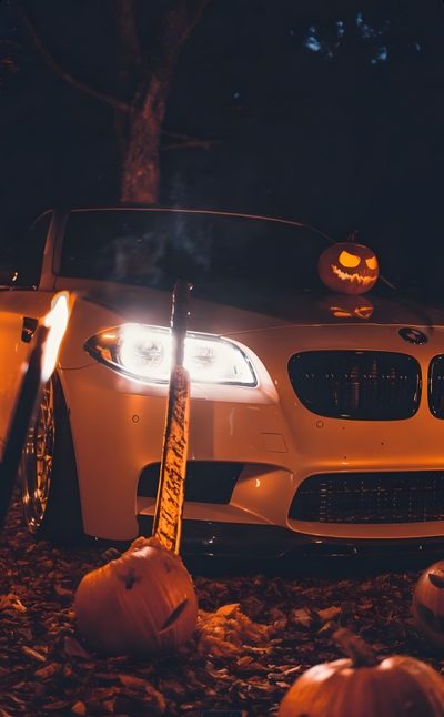a white car with pumpkins on the hood in front of it and two jack - o'lanterns Bmw Halloween Car With Halloween Pumpkins At Night, Diy Halloween Pumpkin Display, Halloween Car Decoration, dark slate gray