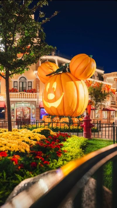 a mickey mouse pumpkin lantern on display in front of a building with flowers and trees Disneyland Halloween Aesthetic Walt Disney World Halloween, Disney Parks Halloween, Disneyland Fall, dark olive green