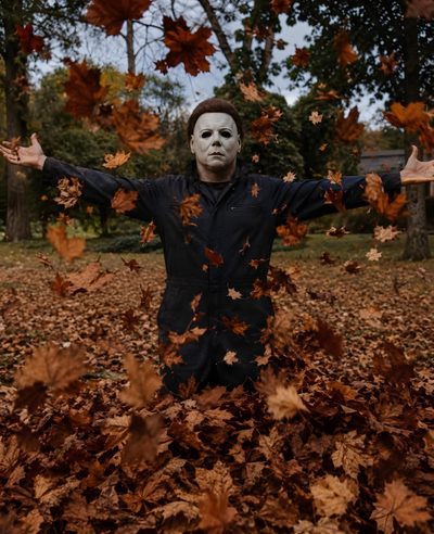 a man wearing a mask standing in leaves with his arms spread out to the side Halloween Michael Myers Iphone Michele Myers, Halloween Movies Aesthetic, Halloween Michael Myers, maroon