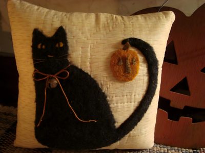 a black cat sitting on top of a pillow next to a pumpkin and a button Halloween Black Cat Pillow Cozy Fall Home Decor Inspiration, Black Cat Pillow With Pumpkin, Diy Halloween Pillow Ideas, maroon