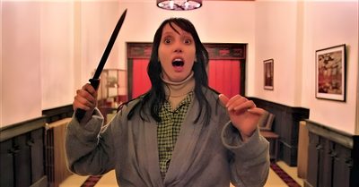 a woman holding two knives in her hands and looking surprised at the camera while standing in a hallway The Shining Laptop Halloween The Shining Wendy Knife, The Shining Stills, Horror Movie Stills Aesthetic, sienna