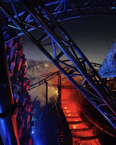 the stairs are lit up with red and blue lights in the dark night time sky Halloween Roller Coaster Halloween Roller Coaster, Dark Themed Amusement Park, Roller Coaster In The Dark, black