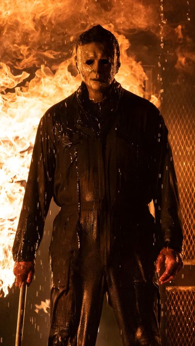 a man standing in front of a fire with his hands on his hips and holding a knife Halloween Kills Michael Myers Halloween Ends, Michael Myers Black Background, Halloween Kills Michael Myers, maroon