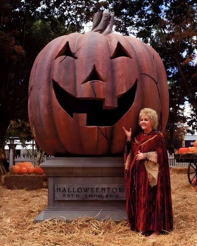 a woman standing next to a carved pumpkin Halloweentown Pumpkin Debbie Reynolds, Halloween Make, Halloween, Halloween Town Movie, saddle brown