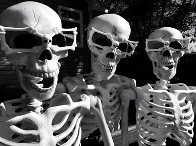 three skeletons sitting on a bench with their heads turned to look like they are holding hands Trio Halloween Diy Halloween Decoration Ideas, Black And White Skeleton Photo, Halloween Skeleton Decor, dark slate gray