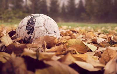 a soccer ball sitting on top of leaves in the middle of an open grass field Halloween Soccer Soccer Ball On Grass, Empty Soccer Field In Autumn, Old Soccer Ball With Roots, sienna