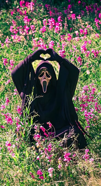 a person wearing a black mask sitting in the middle of a field with pink flowers Halloween Scream Funny Scary, Ghost Faces, Pretty Iphone, Goth, dark olive green