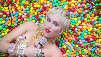 a woman laying on top of a pile of gummy balls with her mouth open Wrecking Ball Halloween Midnight Sky Miley Cyrus Lyrics, Wrecking Ball Cyrus, Miley Cyrus Flowers Music Video, dark khaki