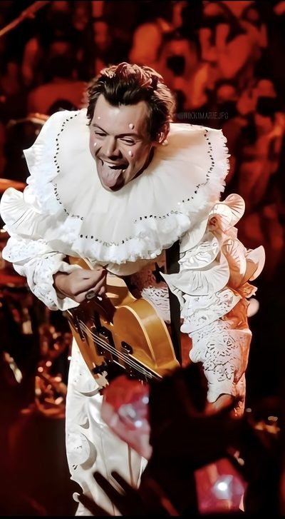 a man that is holding a guitar in his right hand and wearing a white dress Harry Styles Happy Halloween Iphone One Direction Halloween, Harry Styles In Costume, Harry Styles Clown, maroon